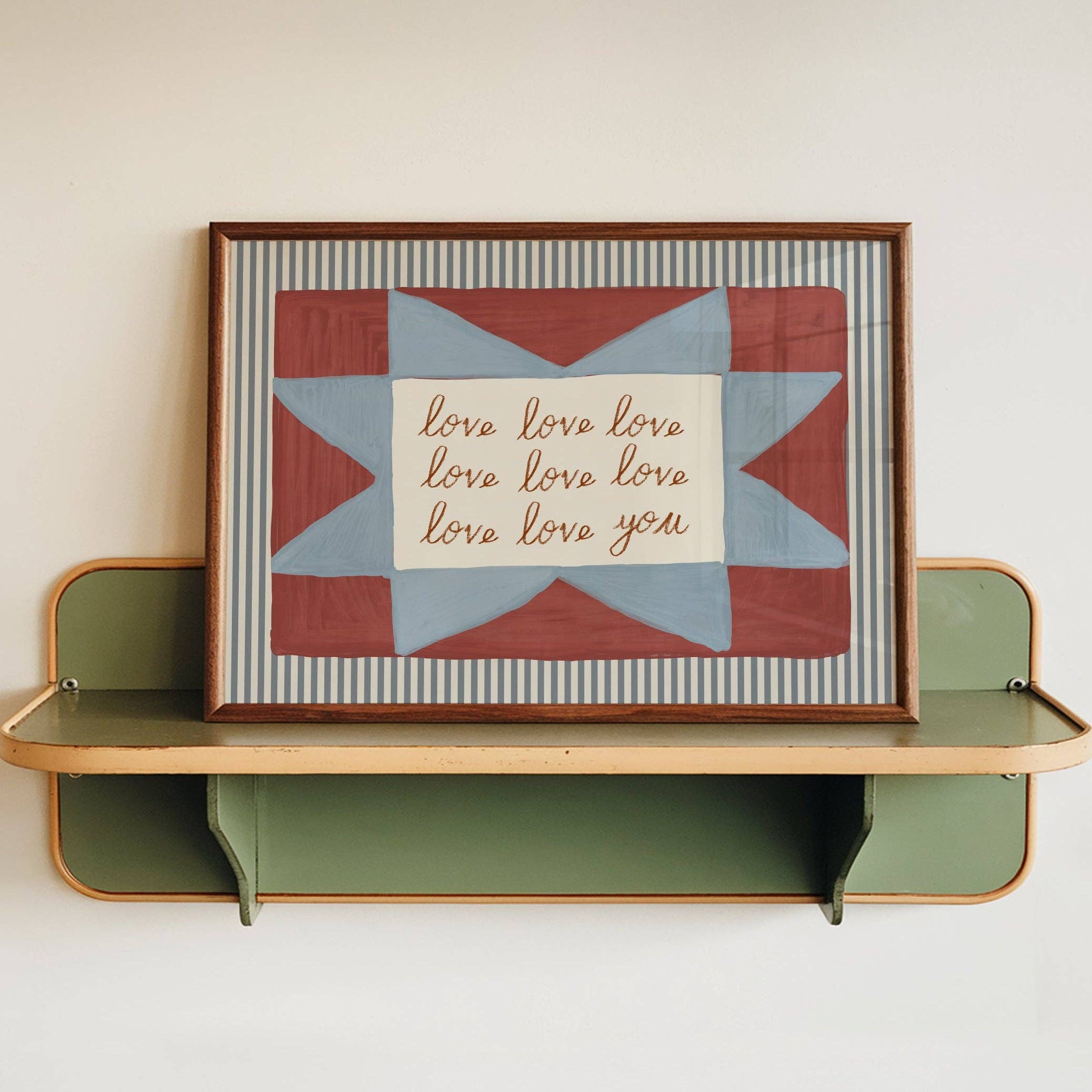 Framed quilt block with 'love you' text on a shelf against a white wall