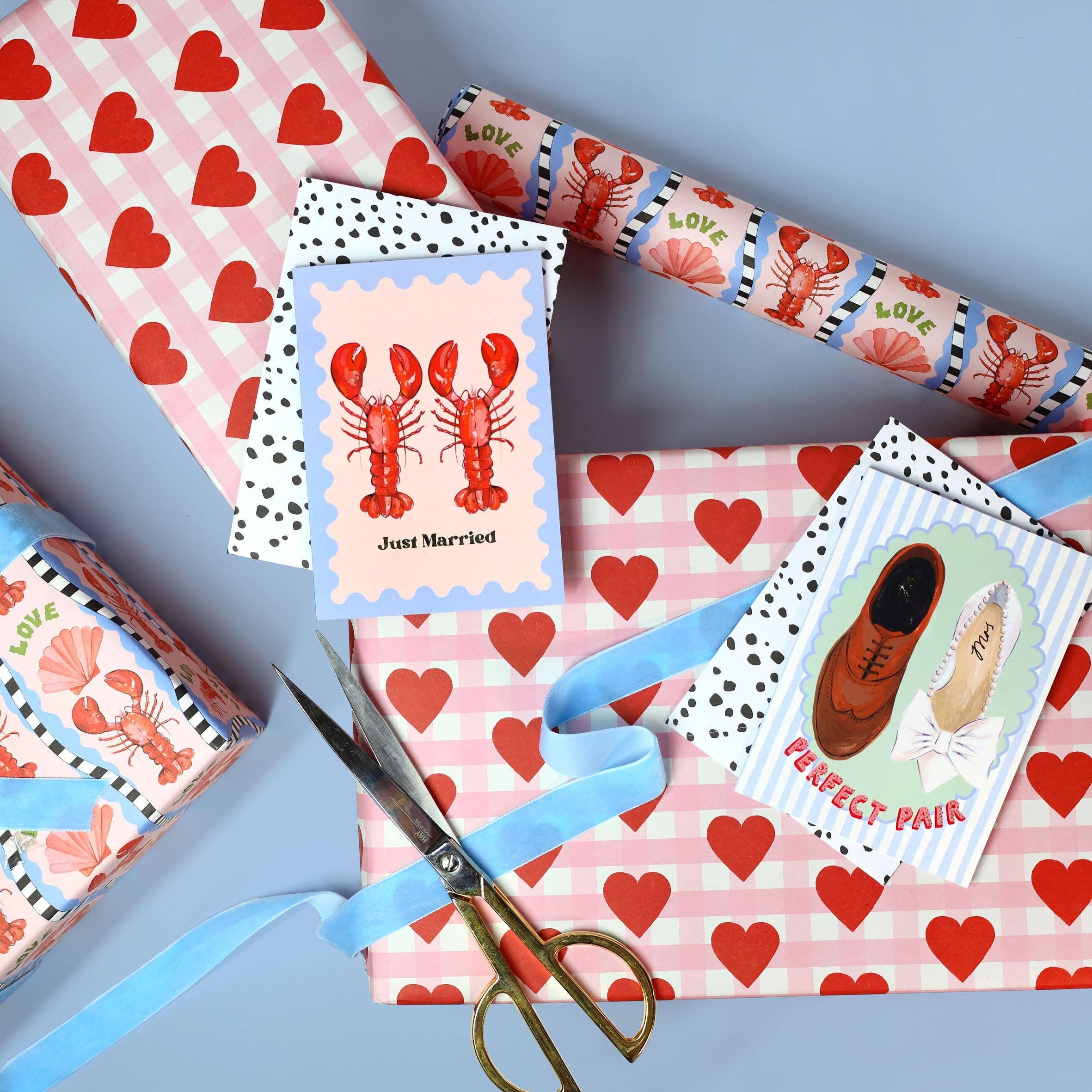 Gift wrap with heart patterns, lobster-themed card, and scissors on a blue background