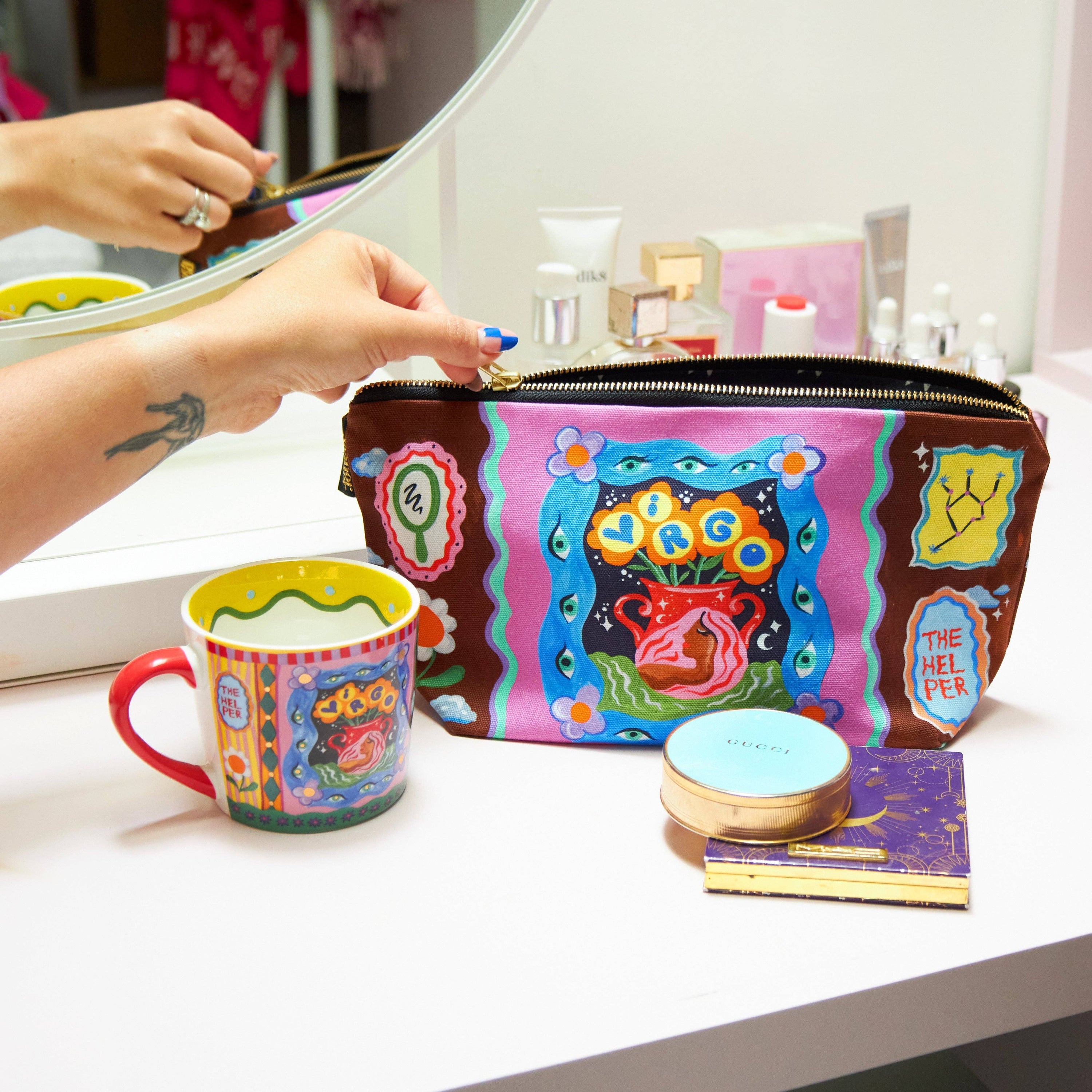 Colourful makeup bag and mug with artistic design on a vanity table.