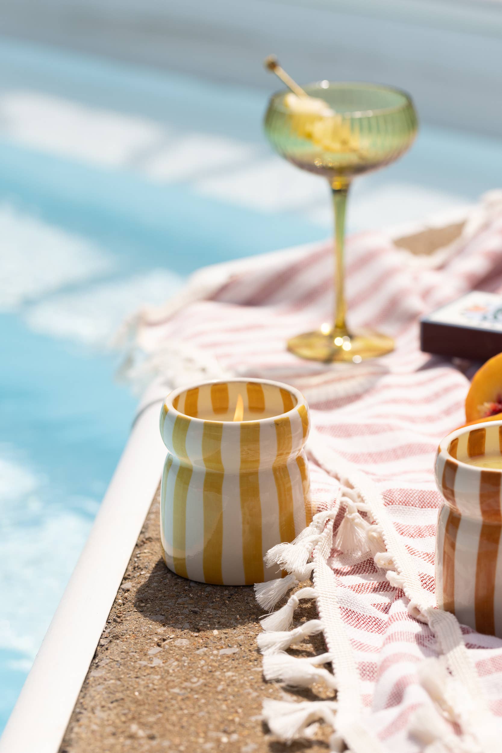 Yellow striped candle and glass with fruit on a poolside tablecloth.