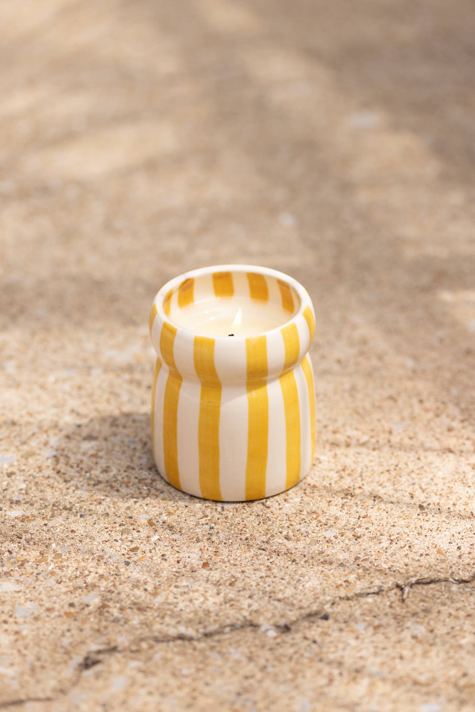 Yellow and white striped ceramic container on sand