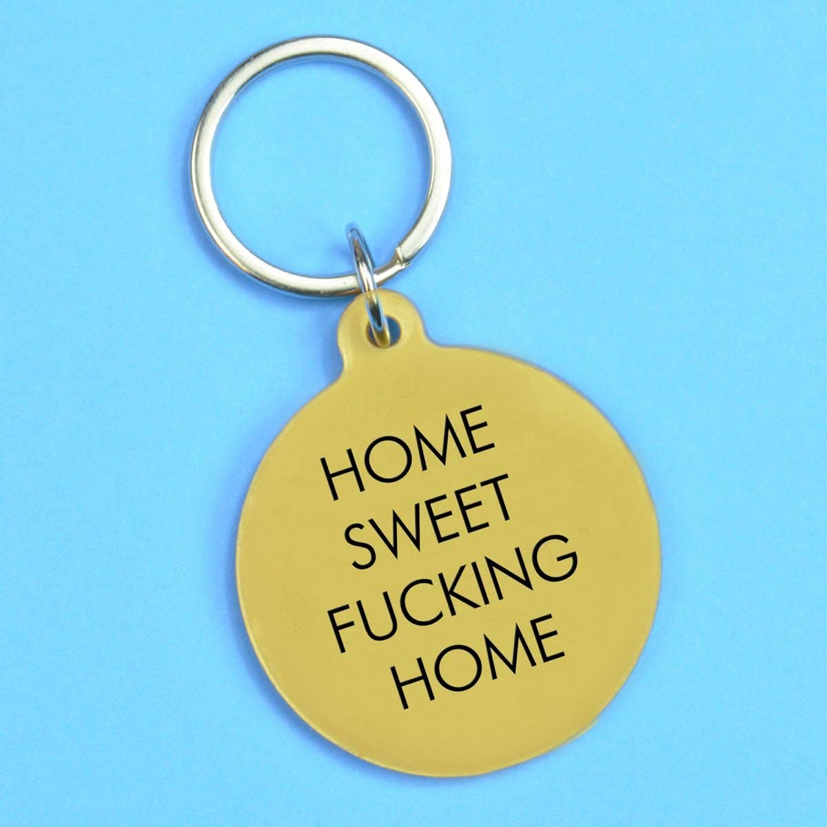 Gold keychain with 'HOME SWEET FUCKING HOME' text on a blue background