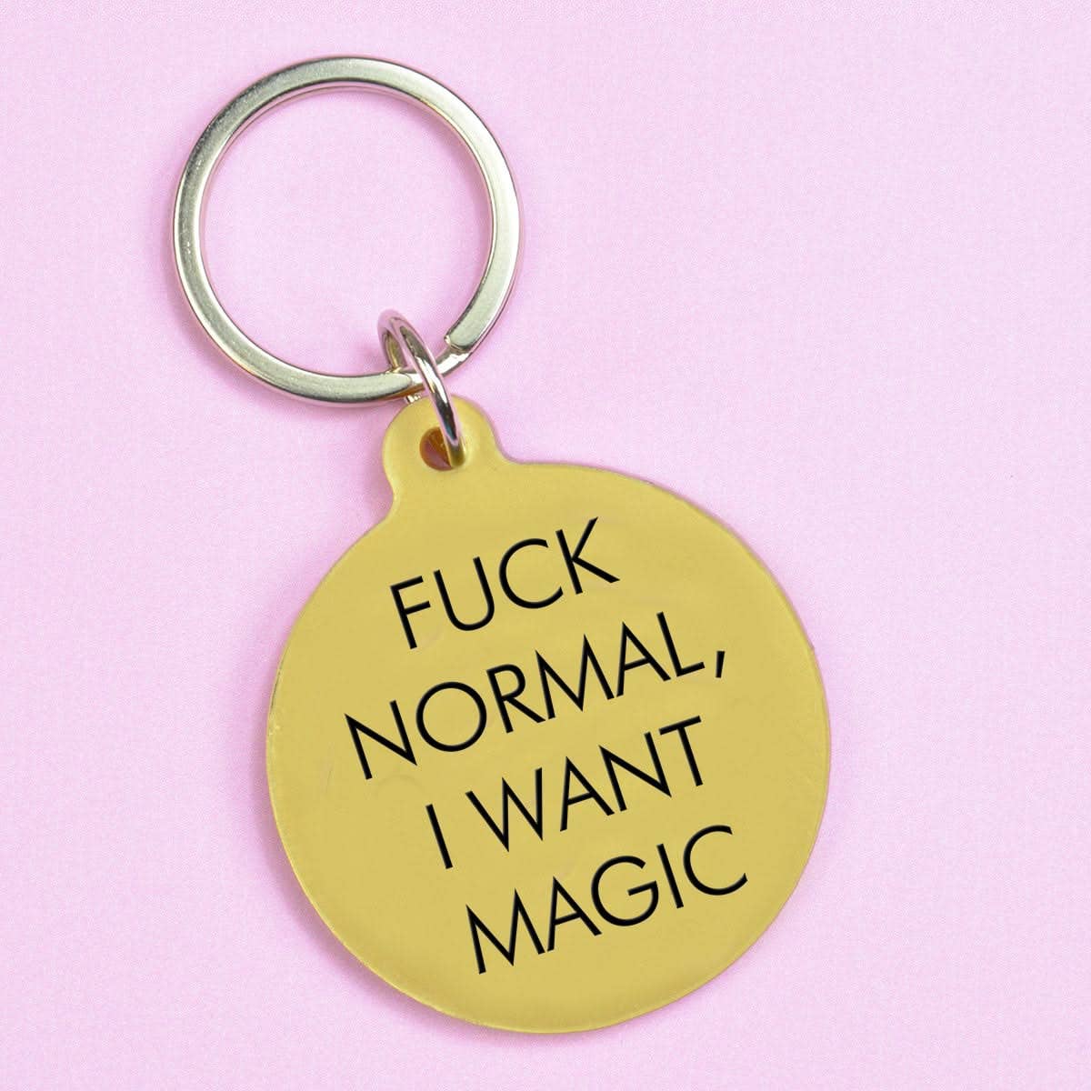 Gold keychain that read "fuck normal I want magic" with black text on a lilac background
