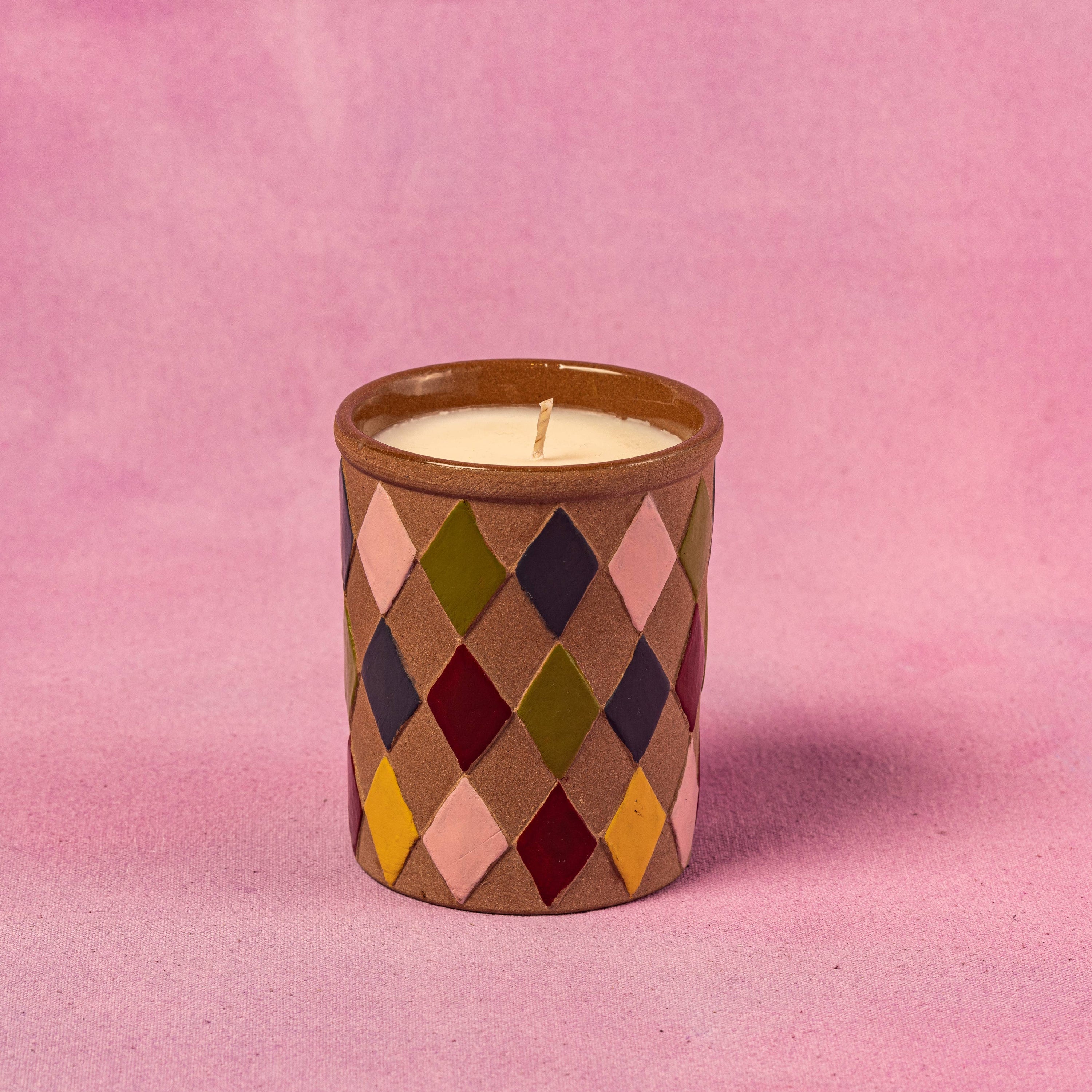 Candle in a diamond patterned container on a pink background