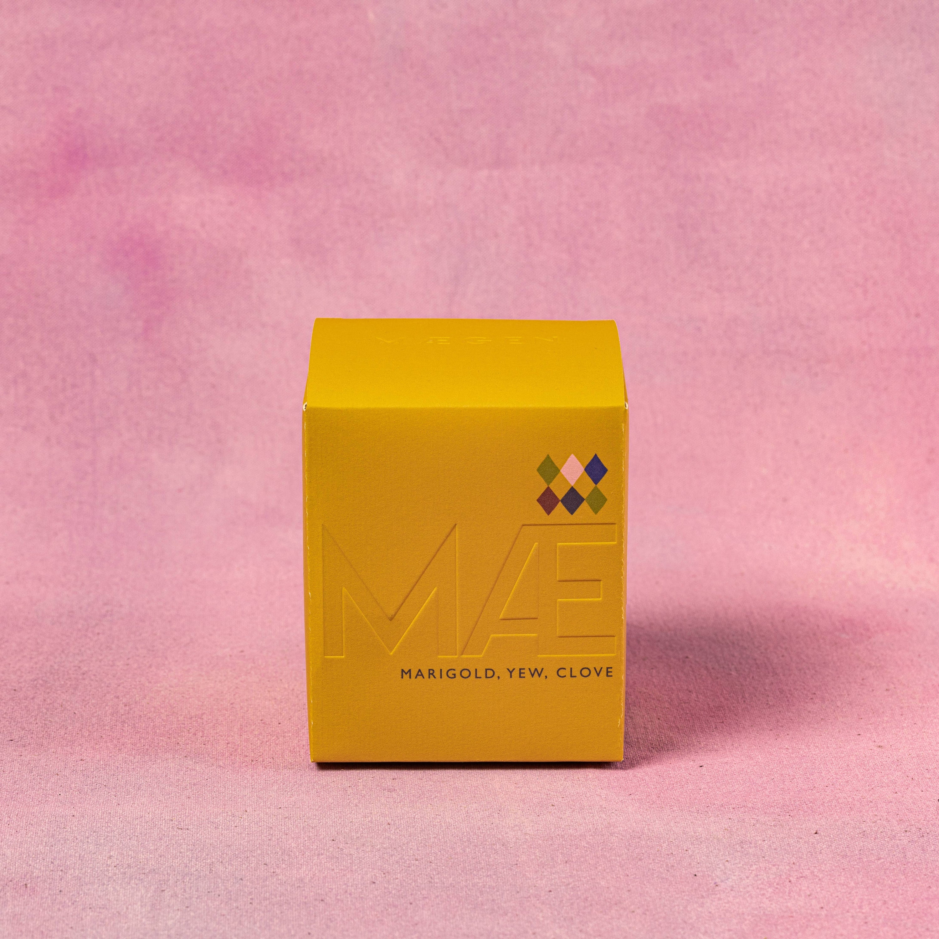 Yellow box with 'MAE'GEN branding on a pink textured background, BOX THE CNALDES COME SIN