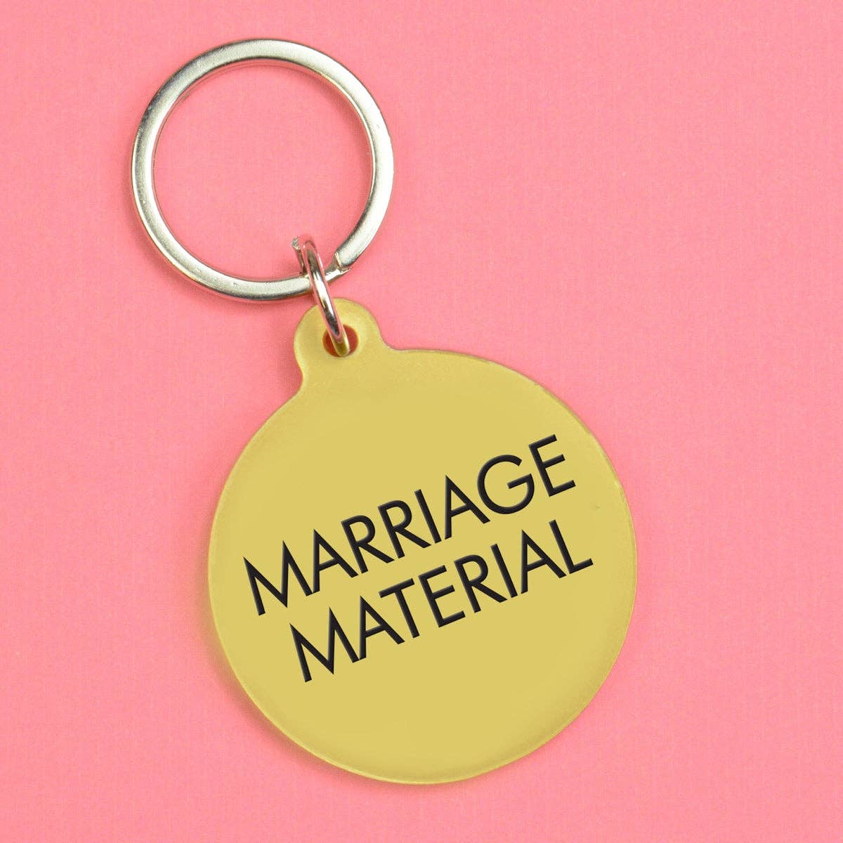 Gold keychain with 'MARRIAGE MATERIAL' text on a pink background