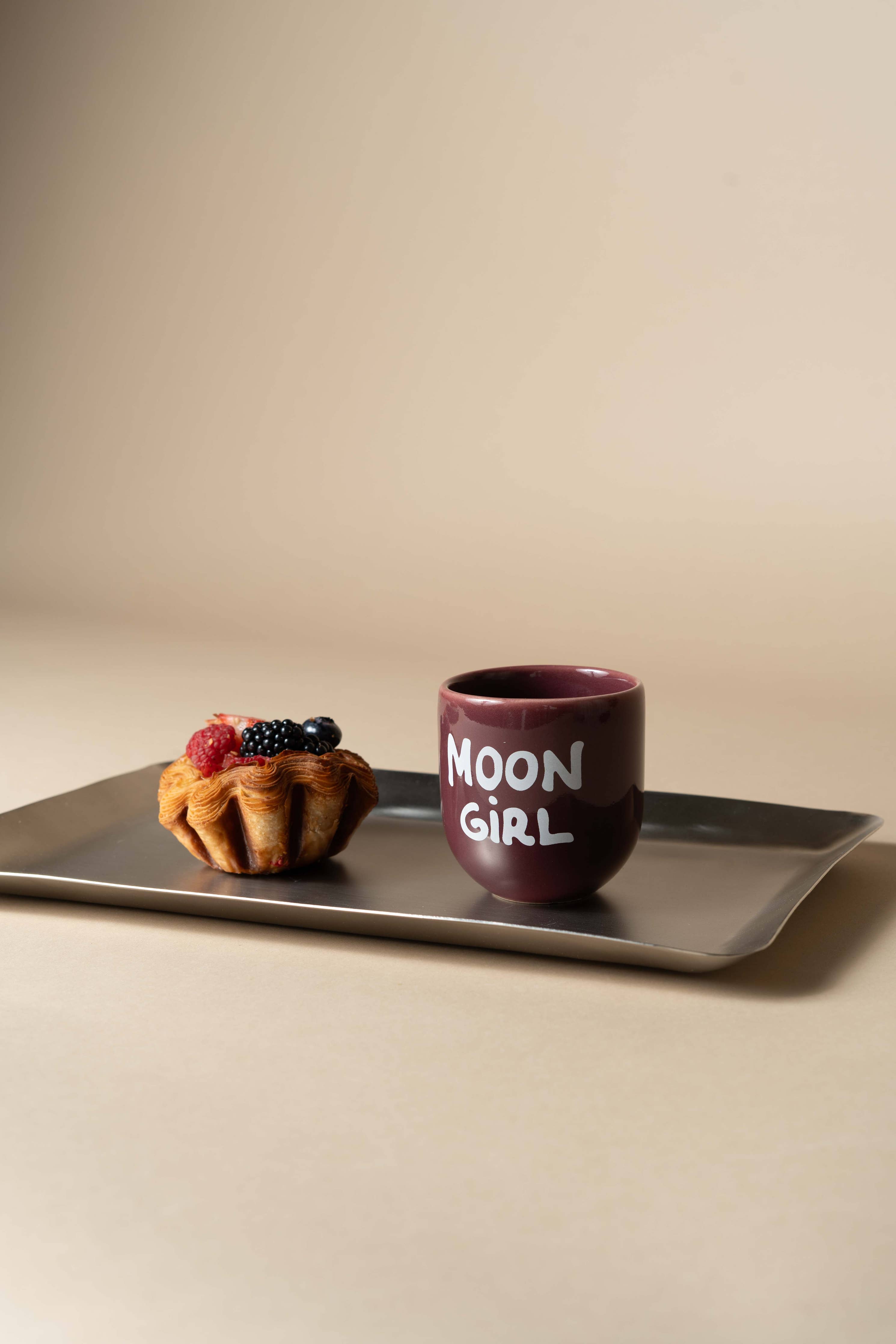 Mug with 'MOON GIRL' text on a tray with a dessert against a beige background