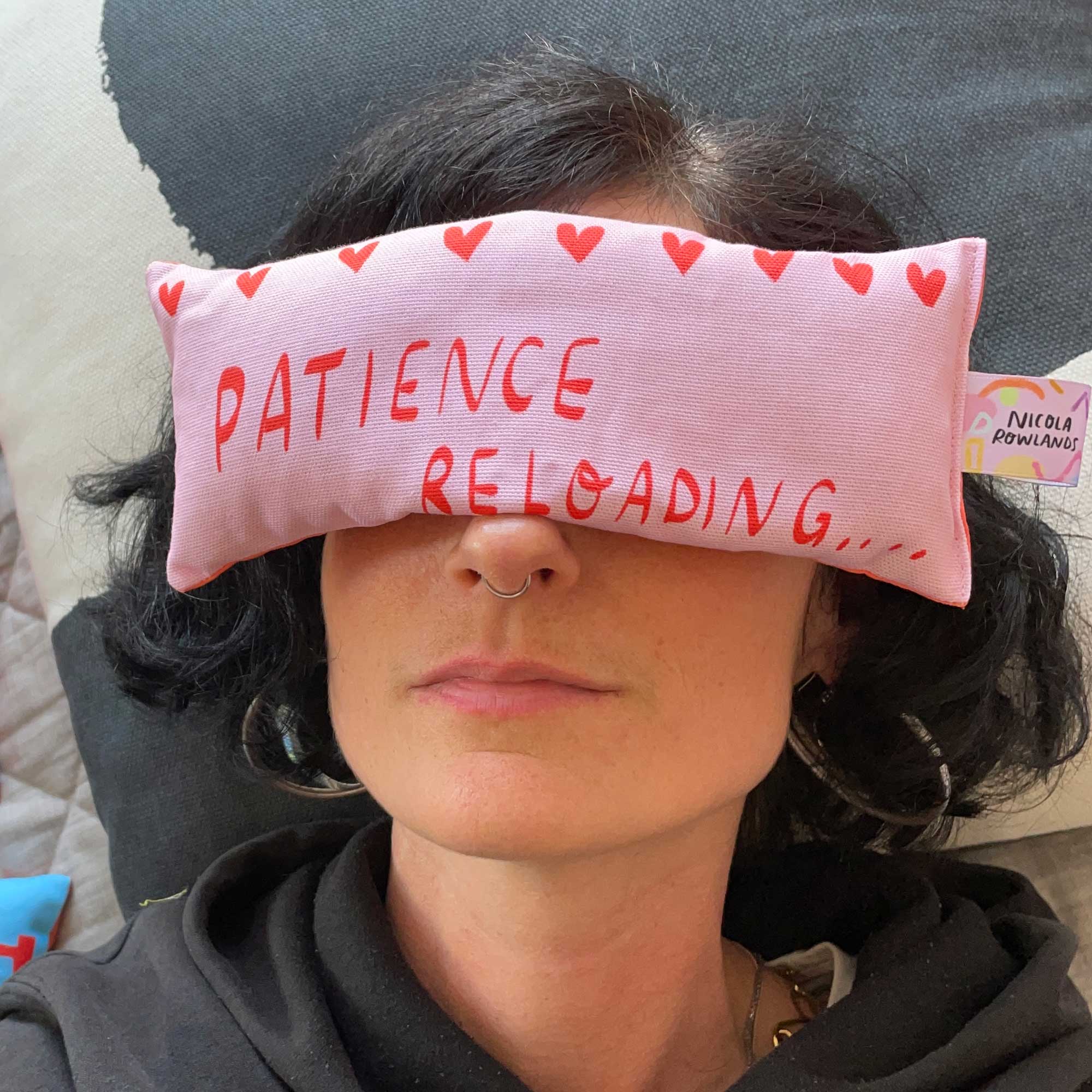 Pink eye pillow being worn y someone meditating, with the text on the eye bag that says " patience reloading
