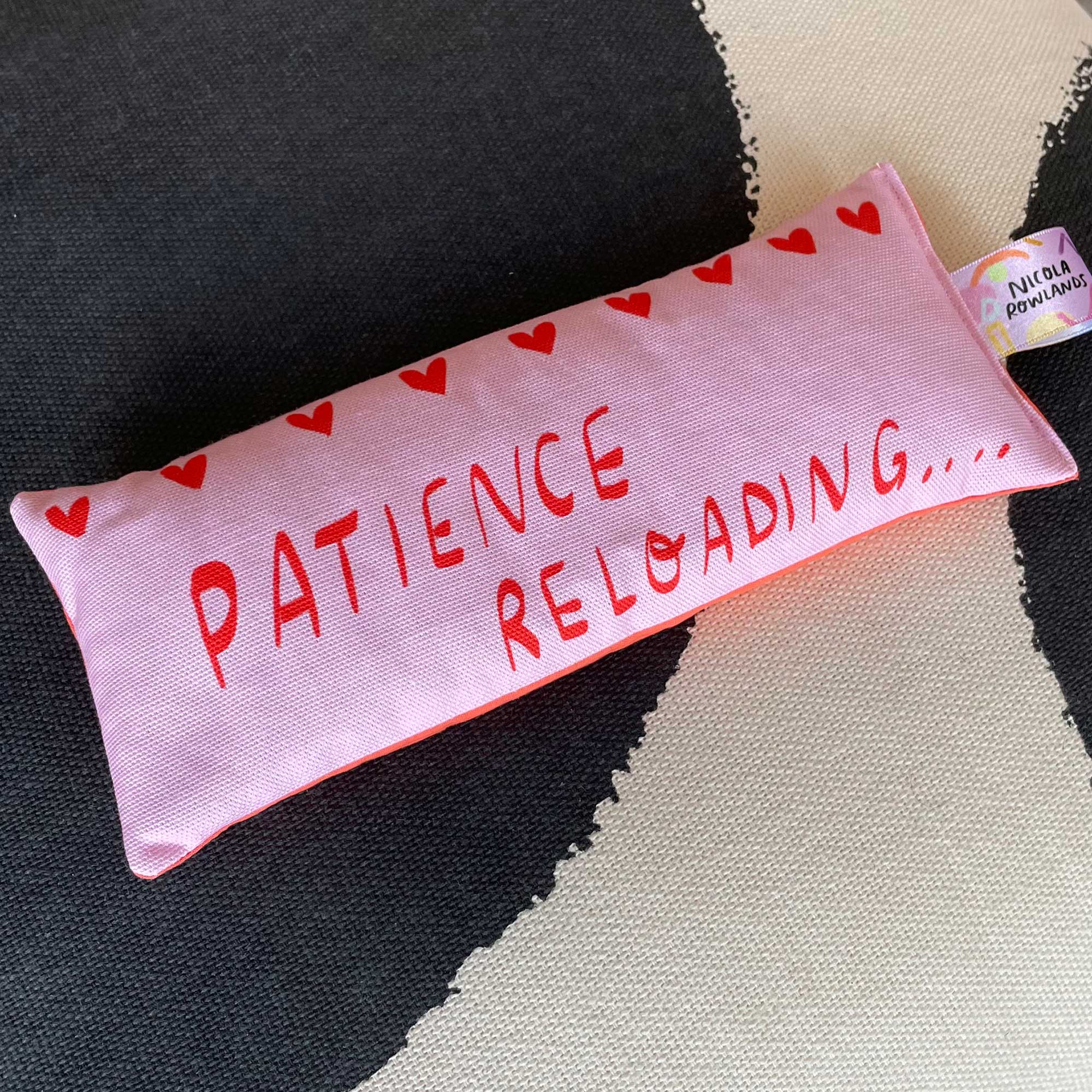 Pink fabric pouch with 'Patience Reloading' text on a textured surface
