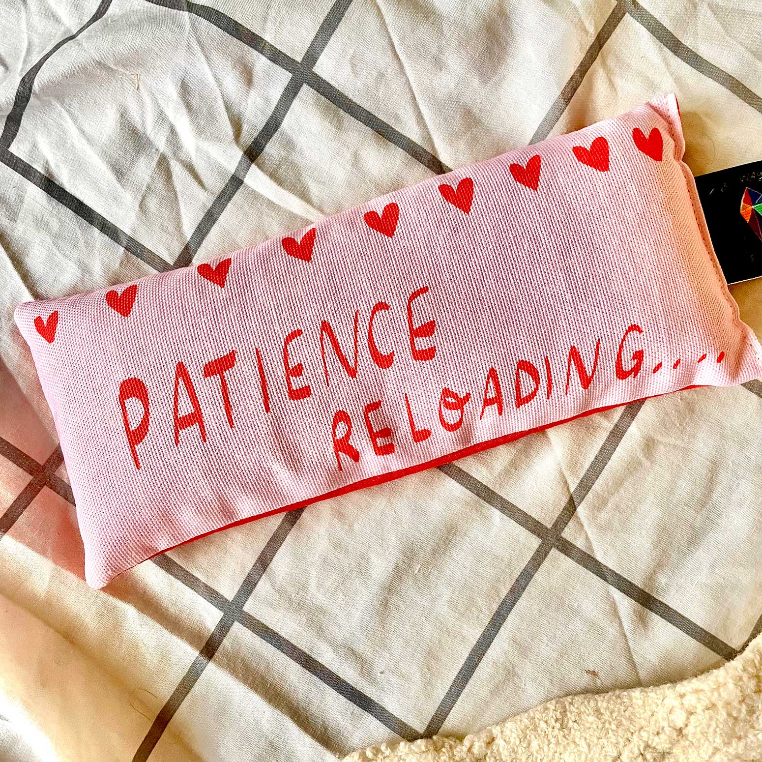 a pink eye pillow with text "Patience reloading" in red on the front,