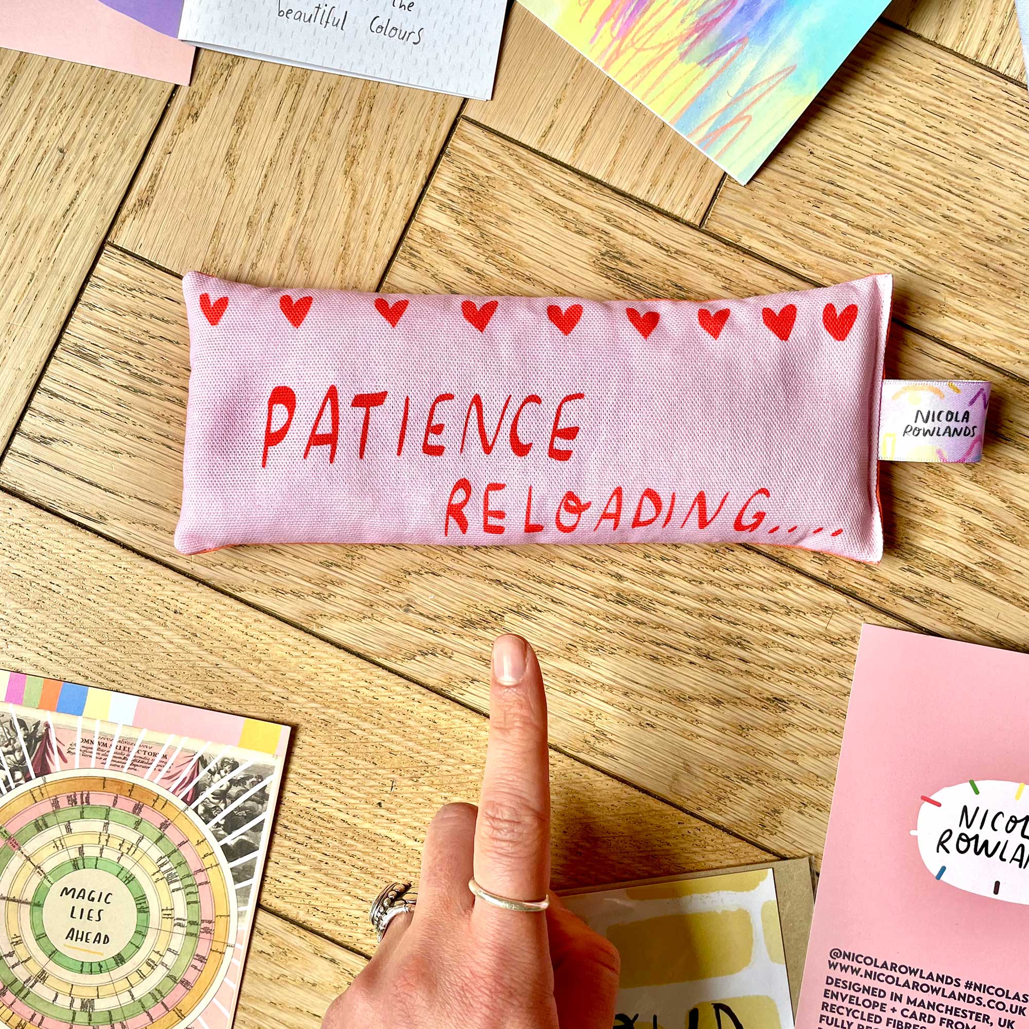 pink eye pillow with text "patience reloading" on a wood desk surface