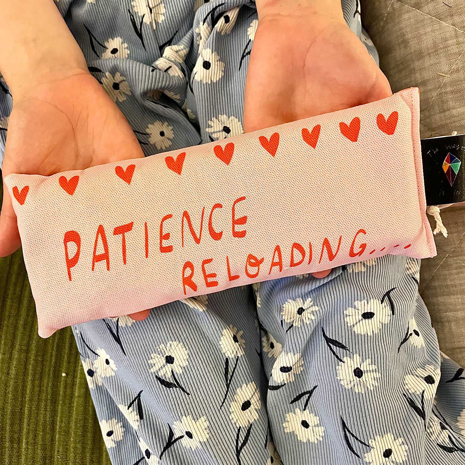 pink eye pillow with text "patience reloading" in the palms of someones hands