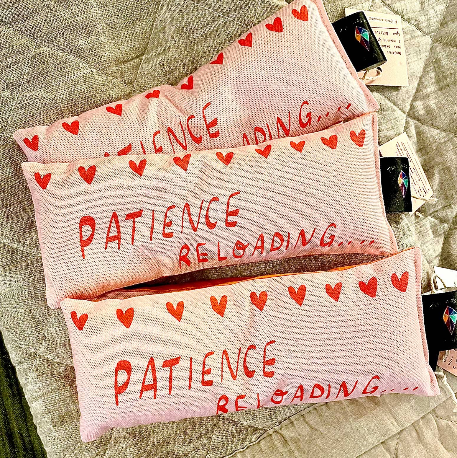 Three pink pouches with 'Patience Reloading' text and red hearts on a textured surface.