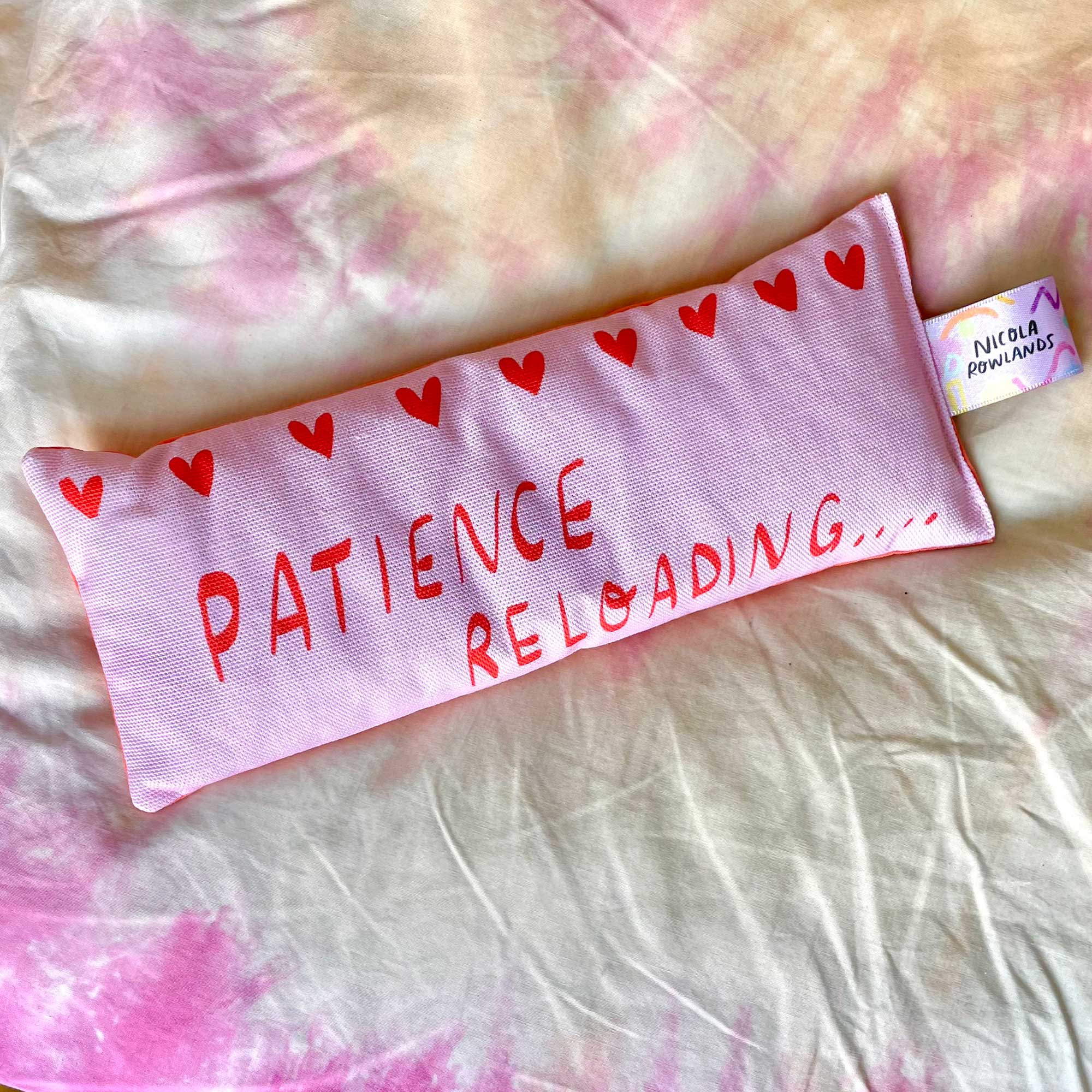 pink eye pillow with red hearts and text "Patience reloading"