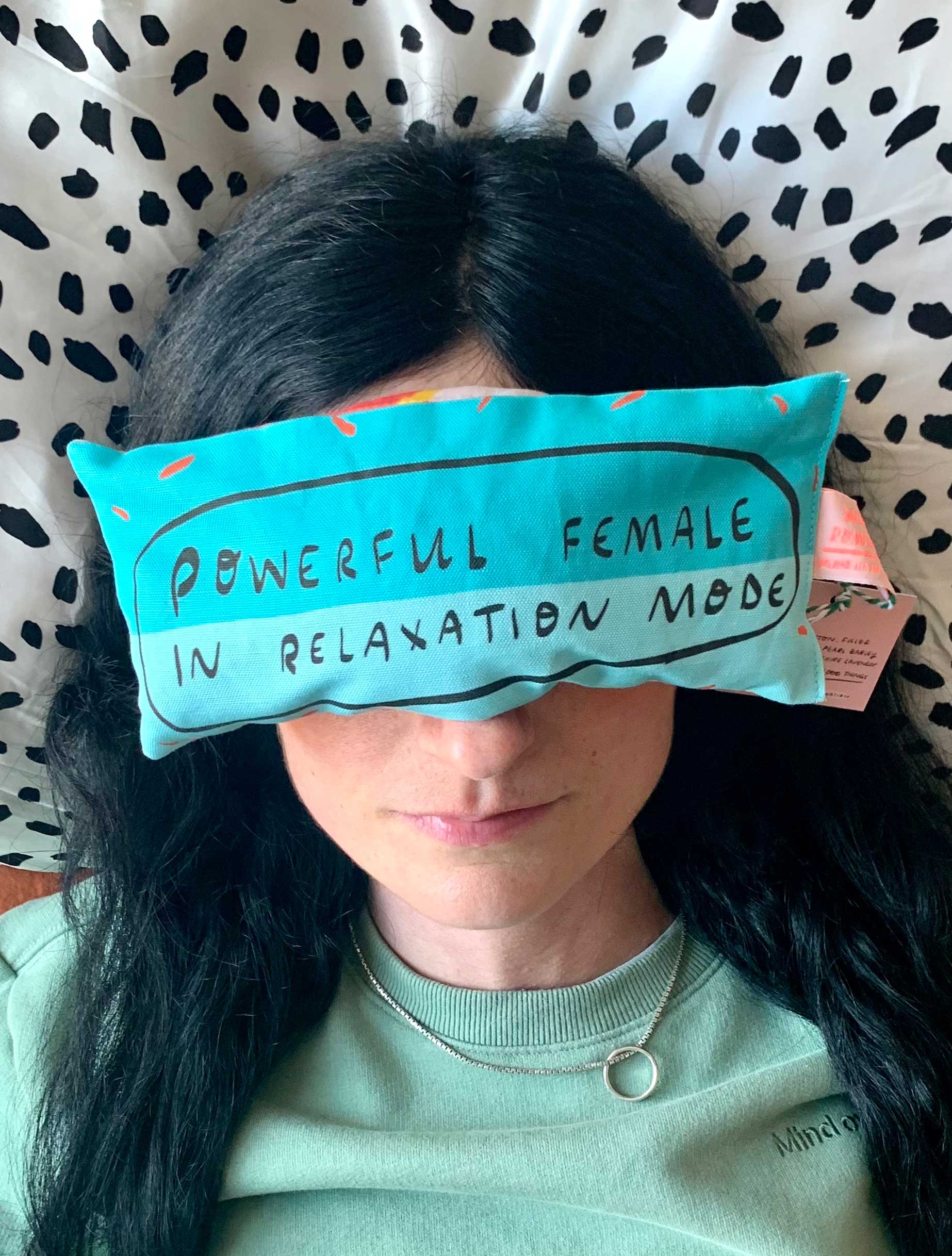 Person wearing a blue eye pillow with text on a patterned background