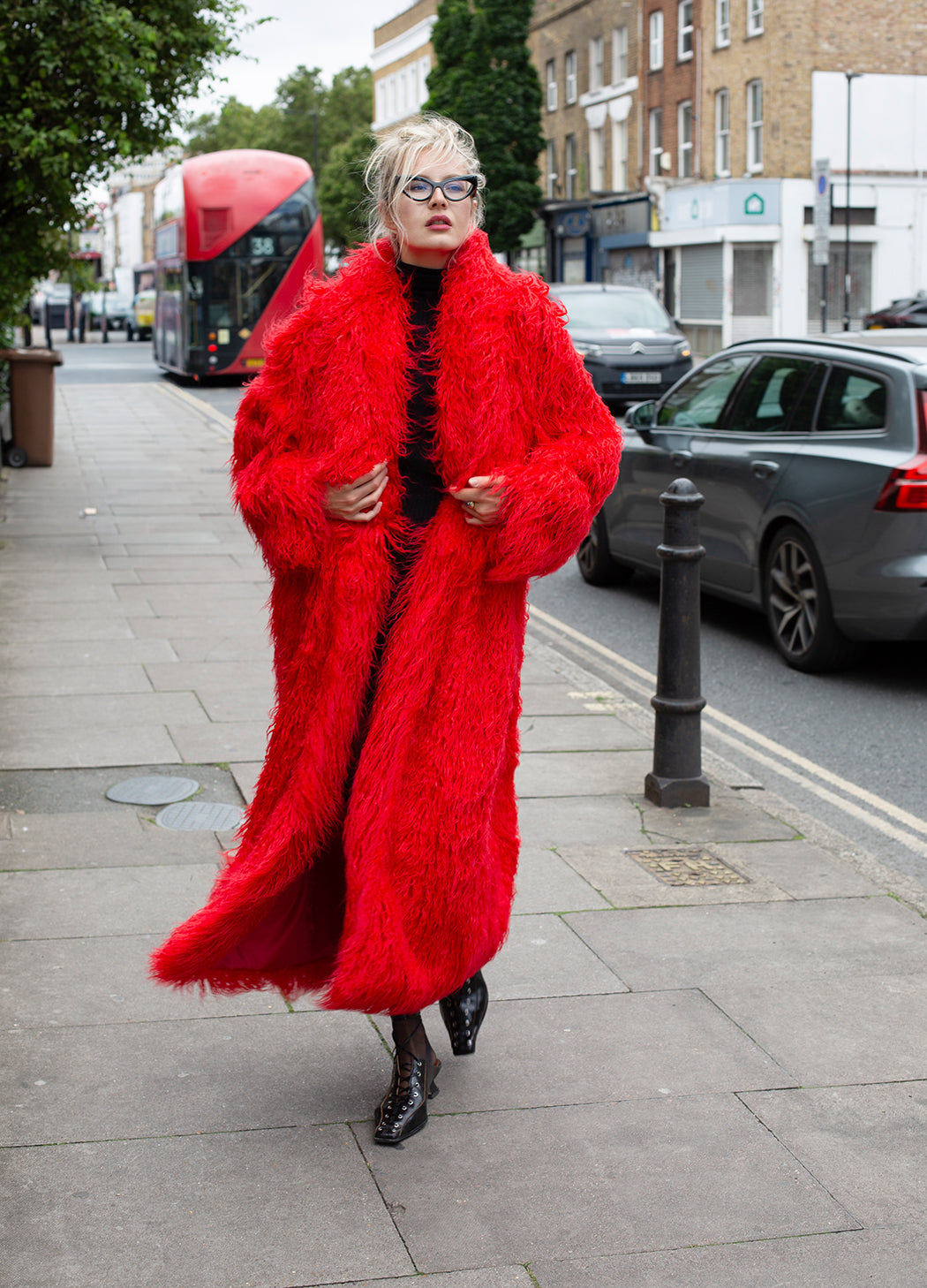 Person wearing a bright red fur coat walking on a city street.