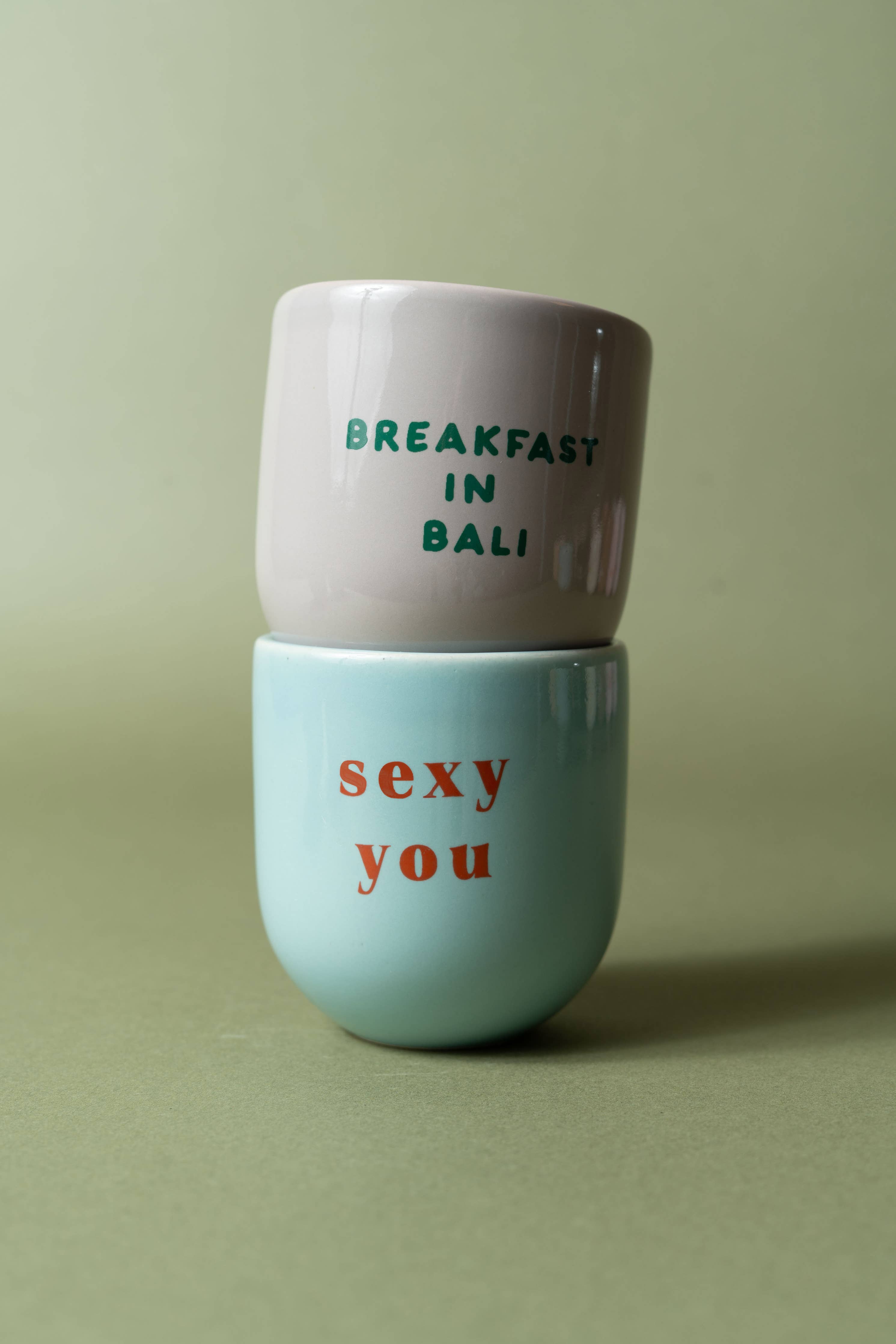 Two stacked ceramic cups with text on a green background