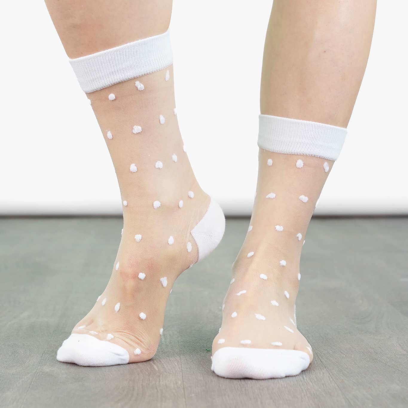Sheer socks with white polka dots and white tops worn by a person on a neutral background