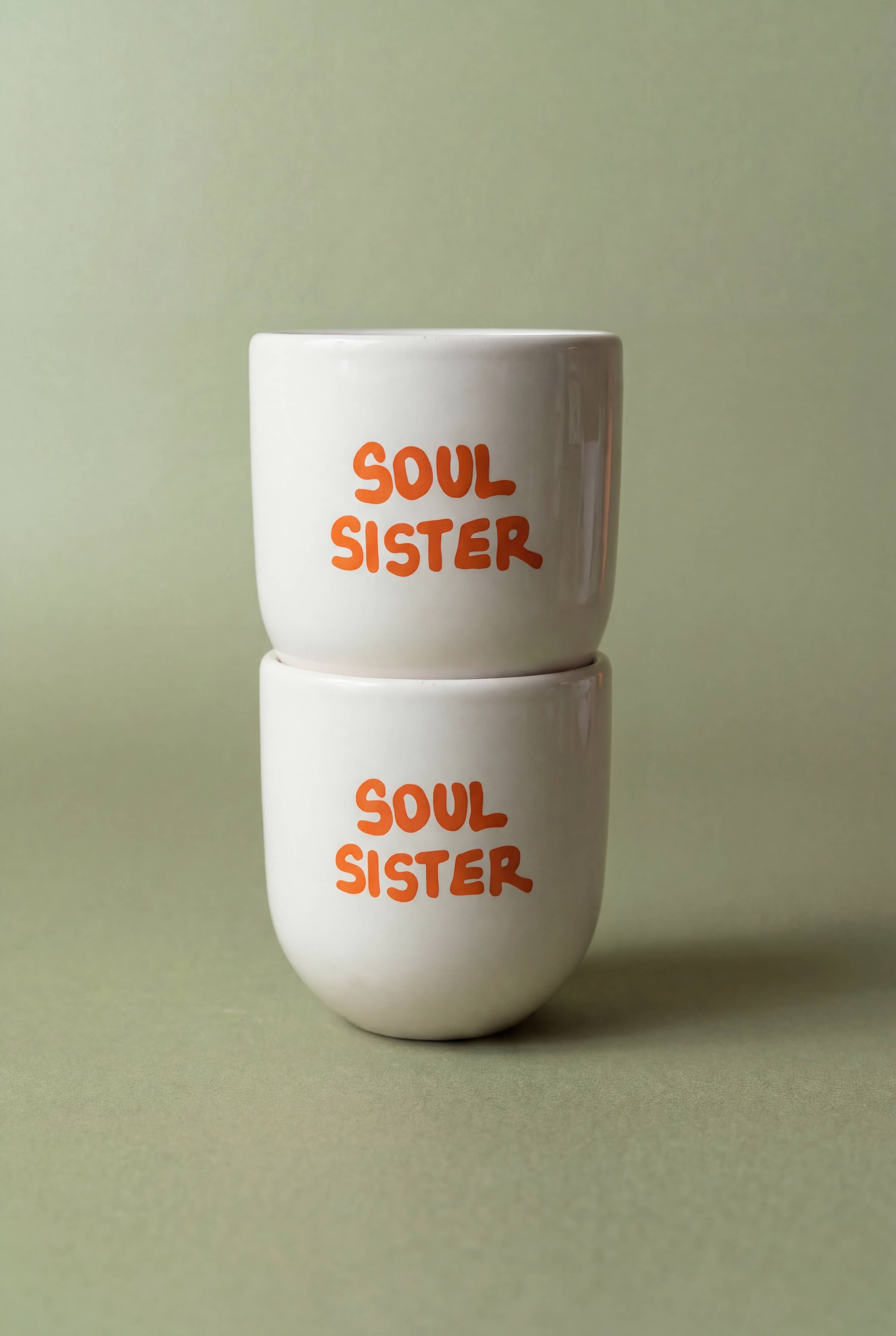 Two white cups with 'Soul Sister' text in orange on a light green background